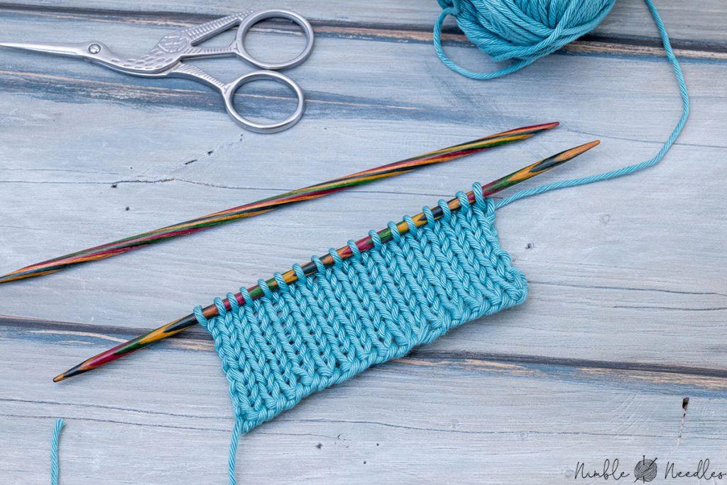 swatch in stockinette stitch with a two needle cast on edge lying on a wooden board