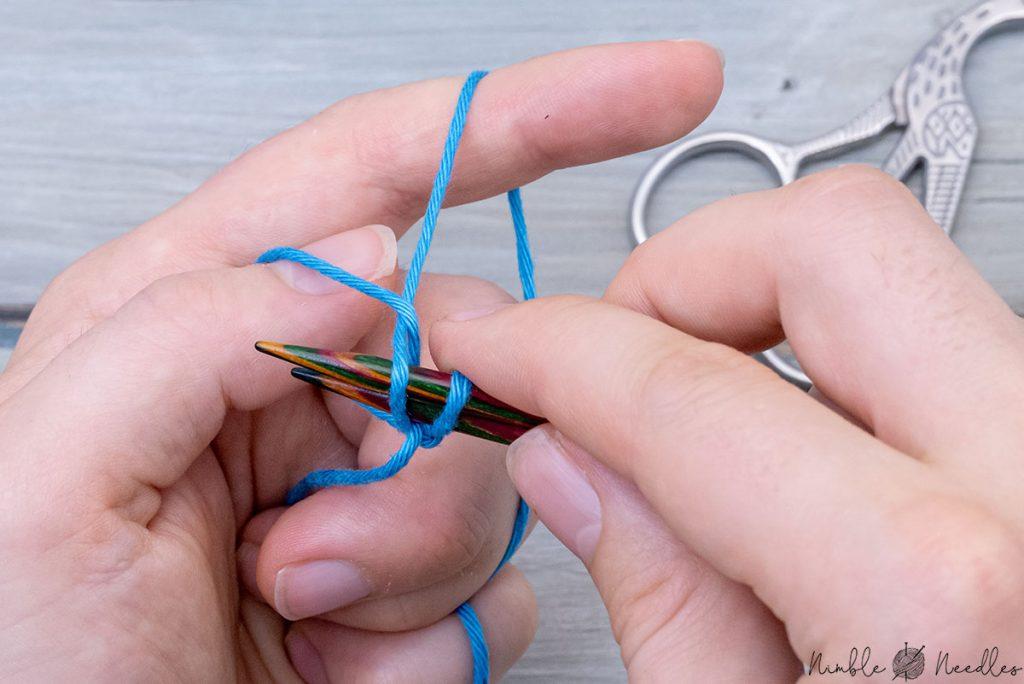 pulling the yarn through the loop around the thumb