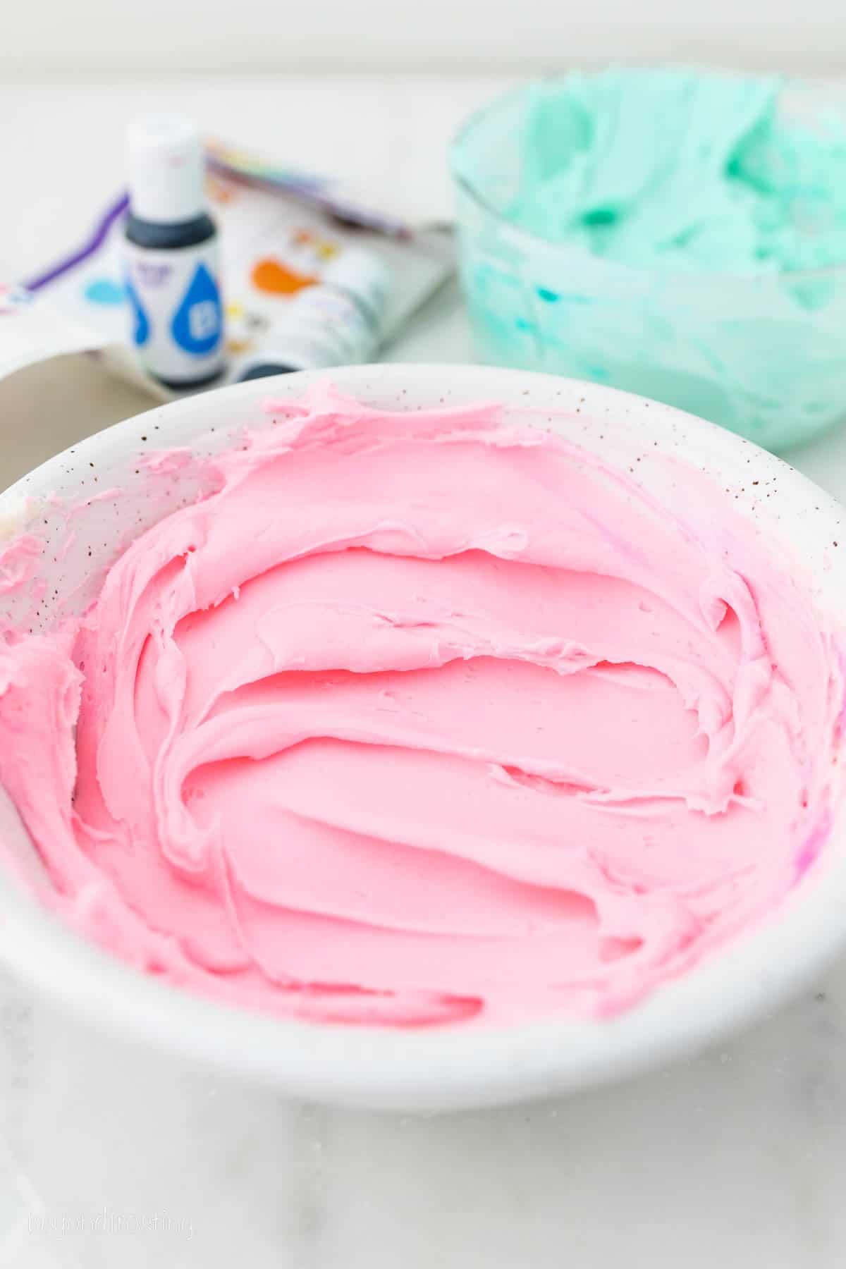 Three piping bags filled with purple, pink, and light turquoise buttercream frosting.