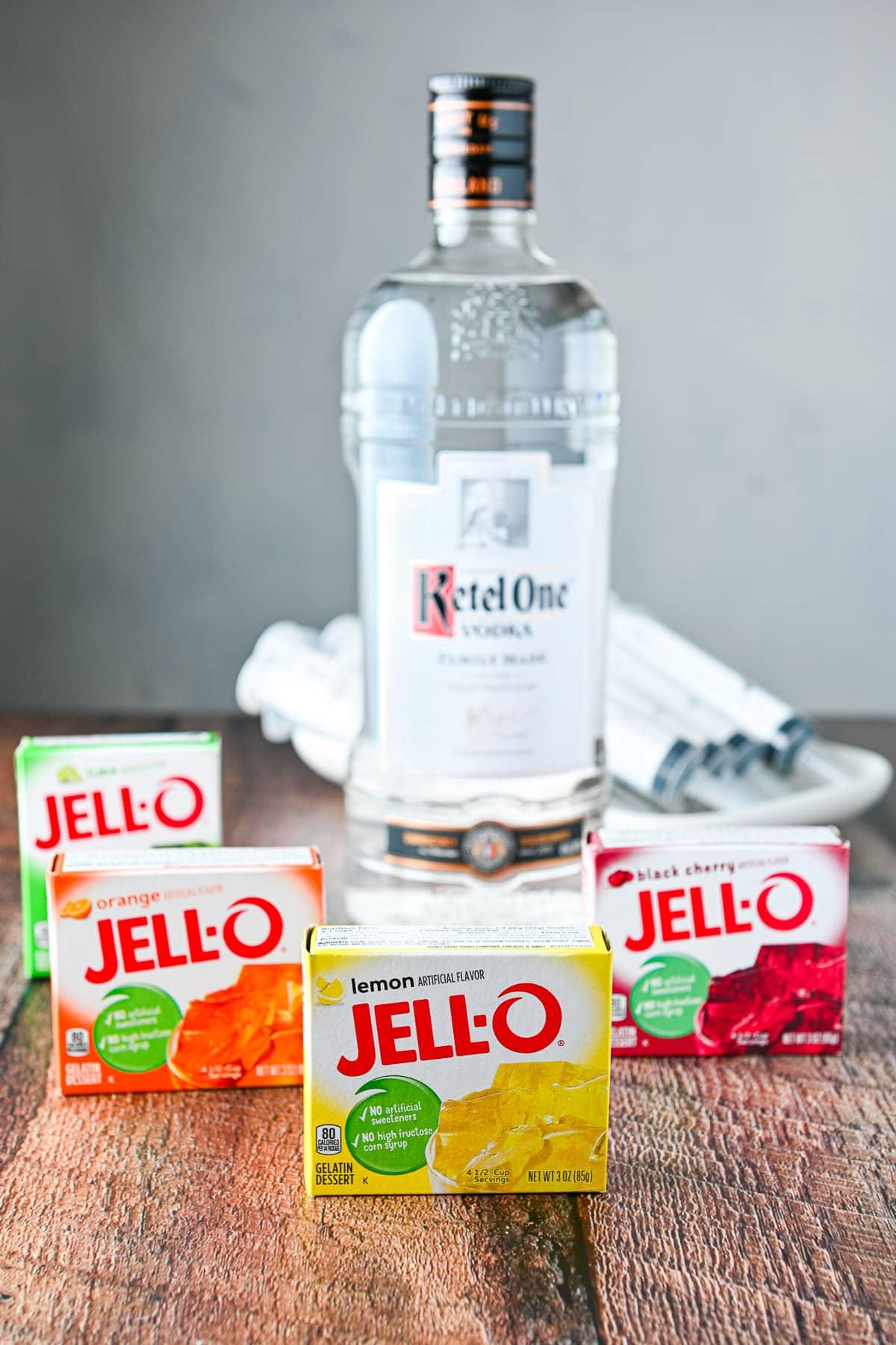 four boxes of different flavored jello on a table with a bottle of vodka