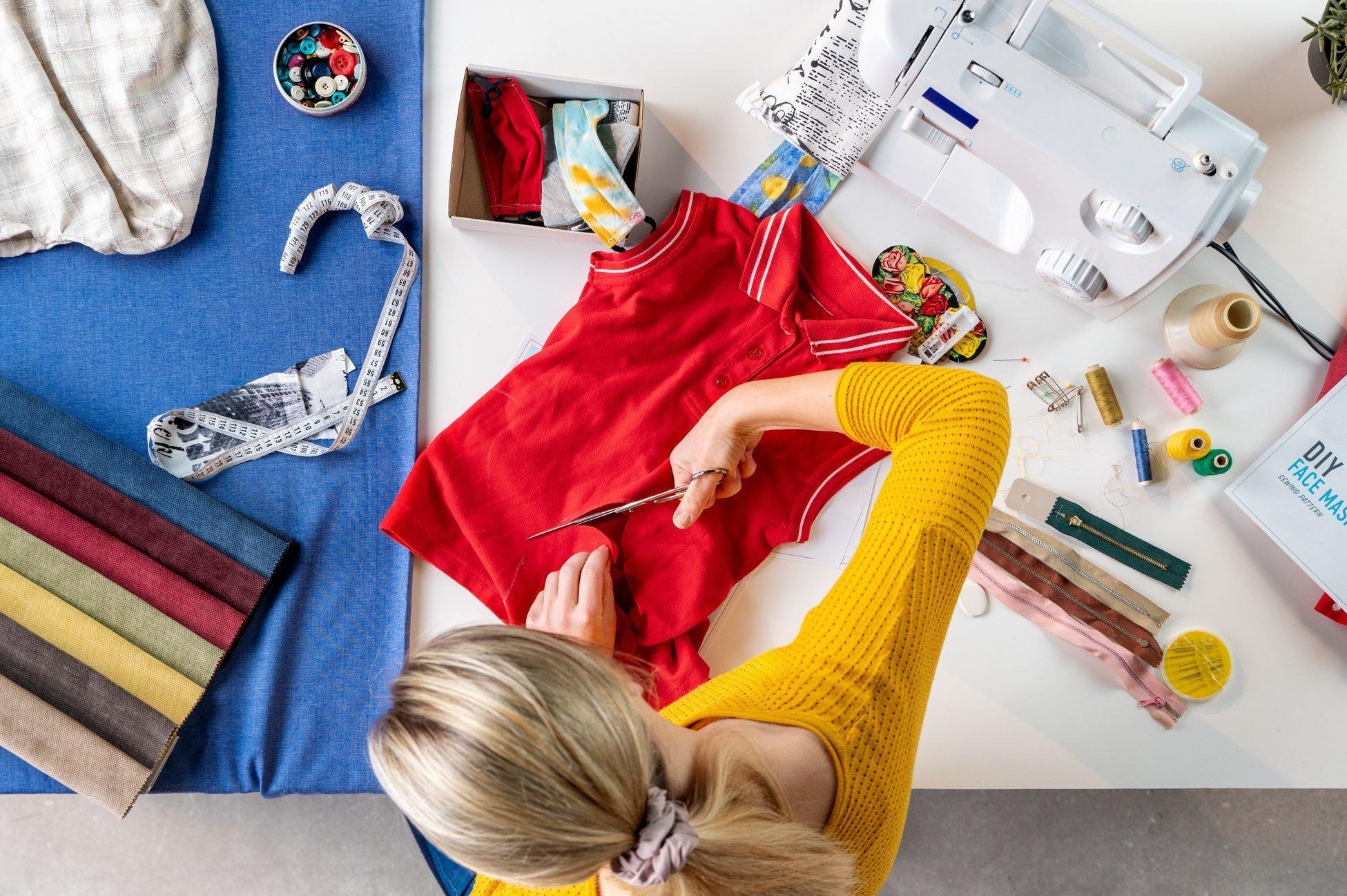 Top view of woman sewing face masks from T-shirt, coronavirus and upcycling concept.