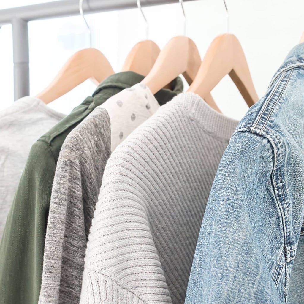 "20 Minimalist Wardrobe Tips: how to create + maintain a minimalist wardrobe" in a white box with A minimalist closet with sweaters and a denim jacket hanging on wooden hangers in the background.