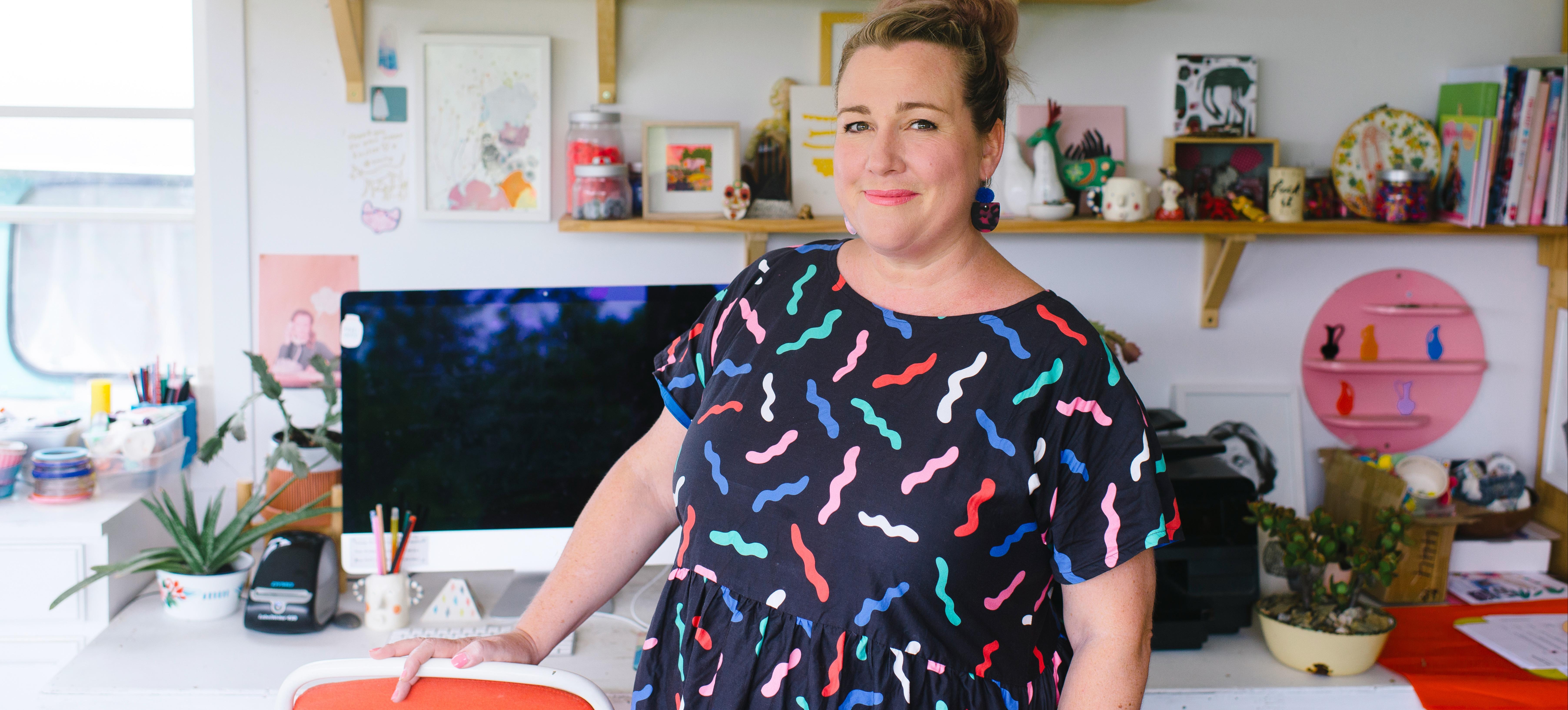 [Image] A woman in a patterned dress stands in front of a desk.