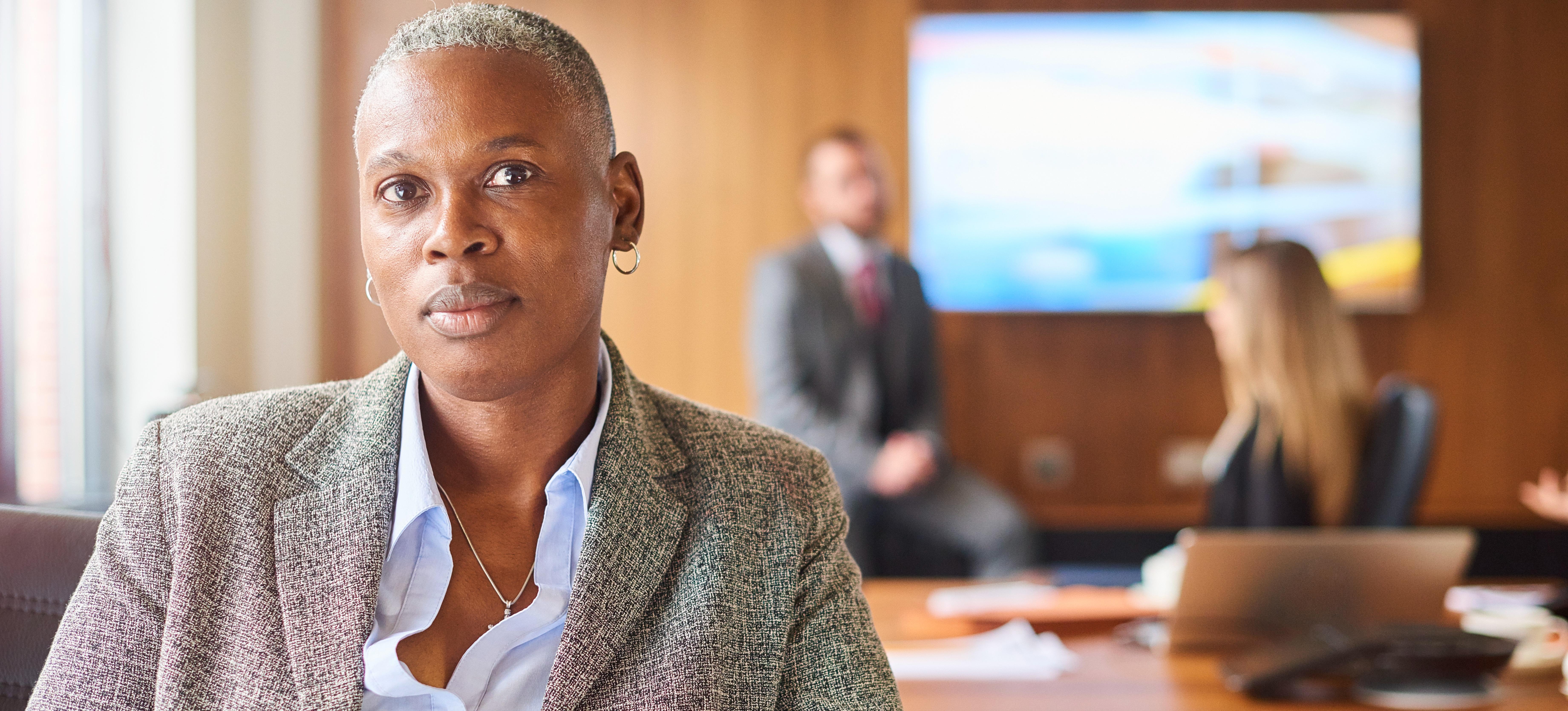 [Image] A woman in a blazer and button-down shirt sits at a conference table.