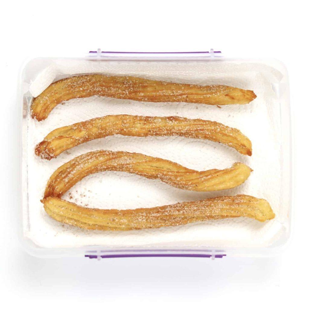 Churros placed inside an open container lined with kitchen roll