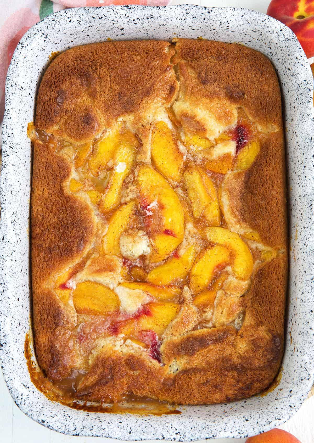 A baked peach cobbler is presented in a casserole dish.