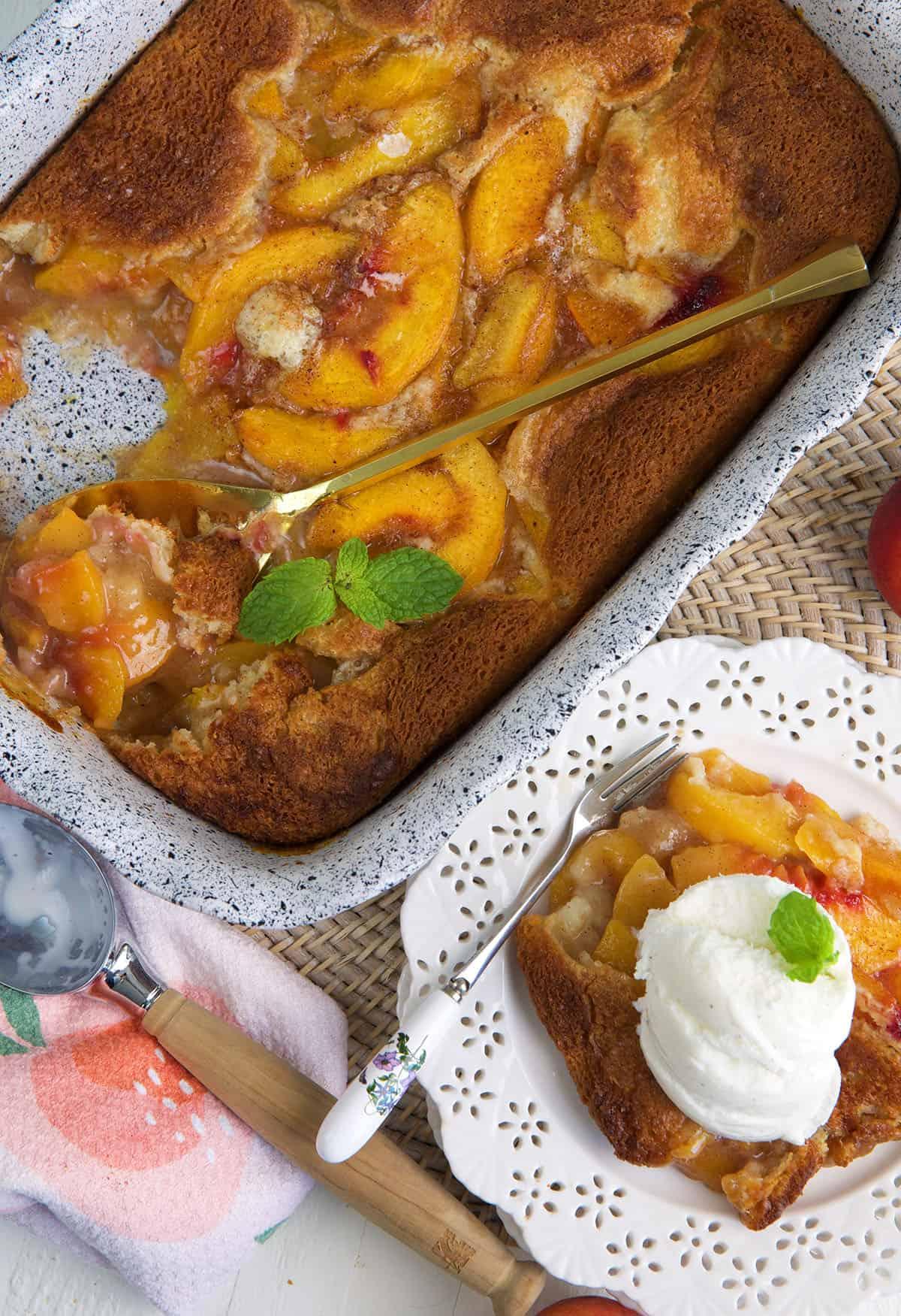 A serving of peach cobbler is presented next to a full casserole dish.