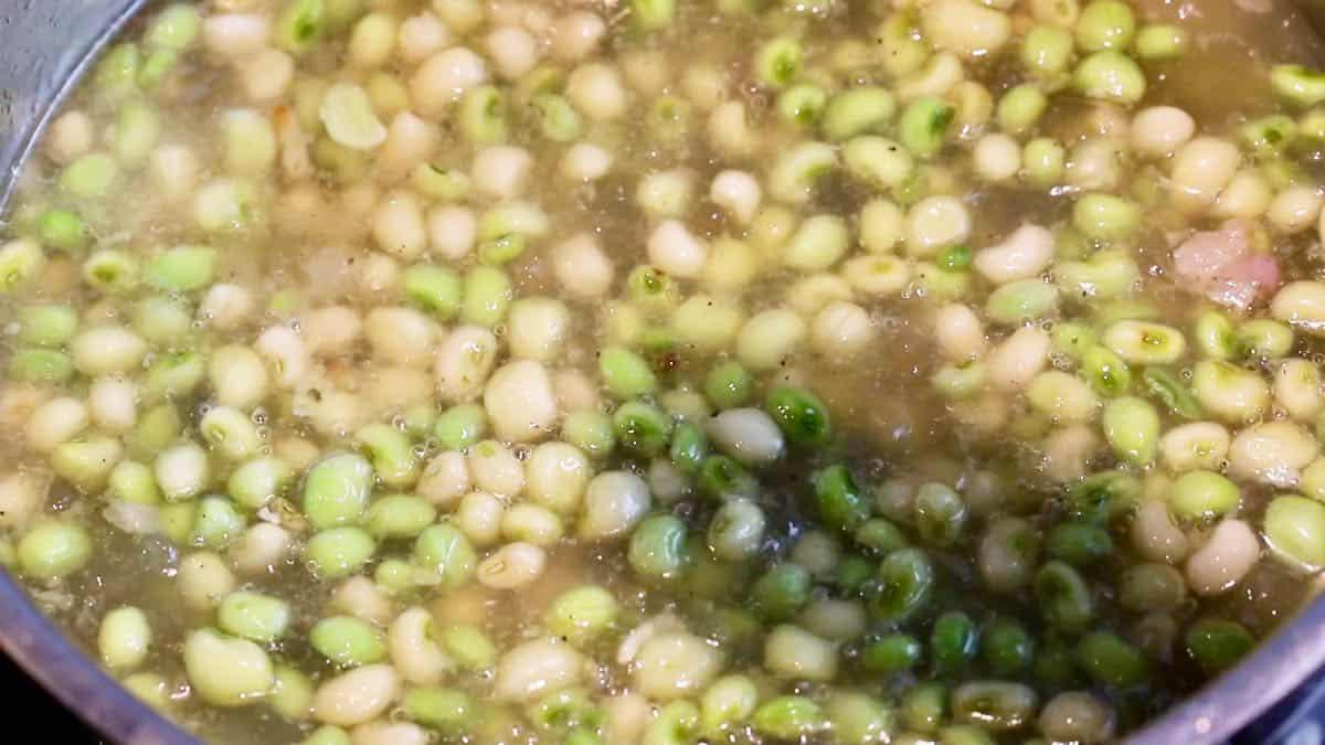 Zipper peas cooking in chicken stock in a saucepan.