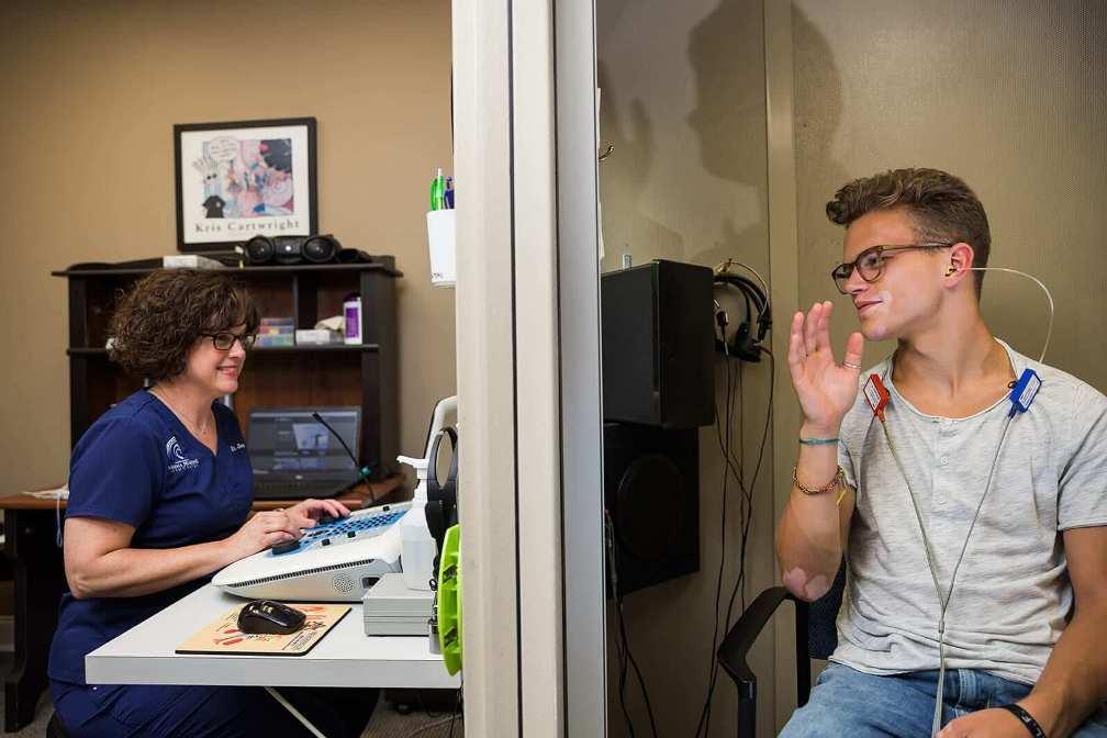 Young patient sitting in a soundproof booth during hearing test with specialist on the other side