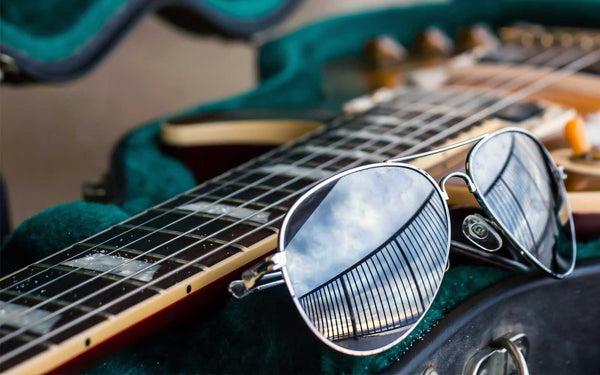 aviator glasses on an open guitar case with sand from the beach