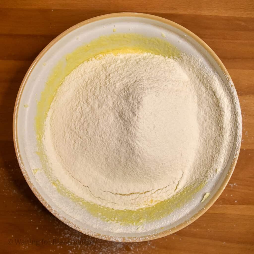 Adding sifted flour and baking powder to batter in large mixing bowl.