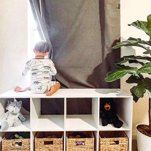 Baby climbing on nursery furniture, playing with blackout curtain in window