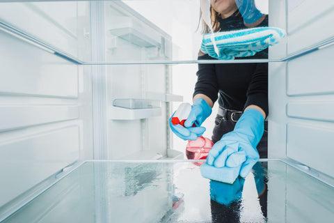 Cropped view of woman in rubber gloves cleaning refrigerator with detergent.