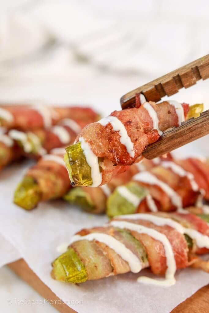 Wooden tongs picking up a bacon wrapped pickle