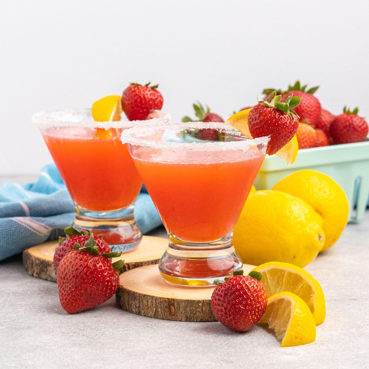 Two strawberry martinis with sugar rim and garnished with a strawberry and lemon wedge.