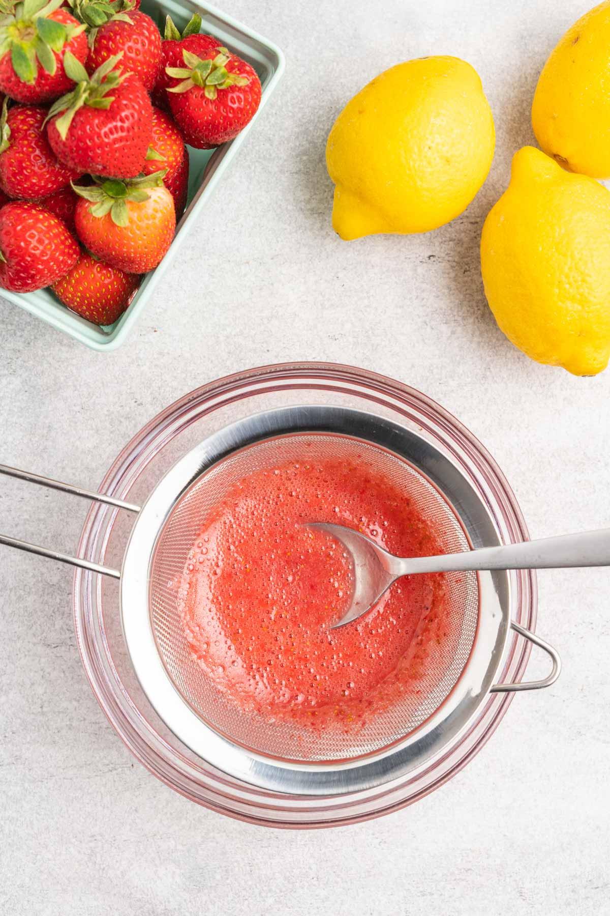 Pureed strawberries in a mesh sieve over a glass bowl.