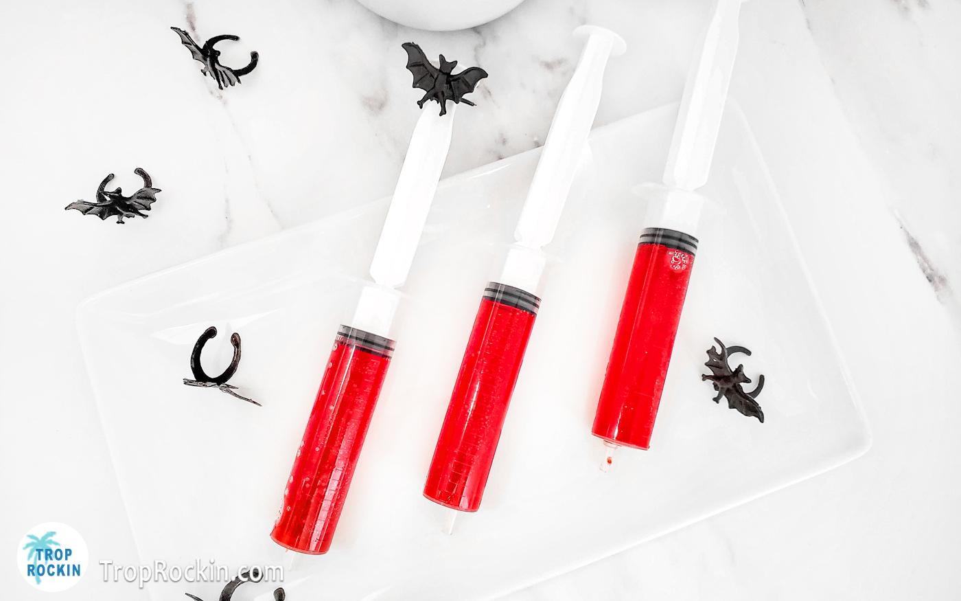 Halloween Shots in Syringes on a serving tray with little plastic black bats for decor.