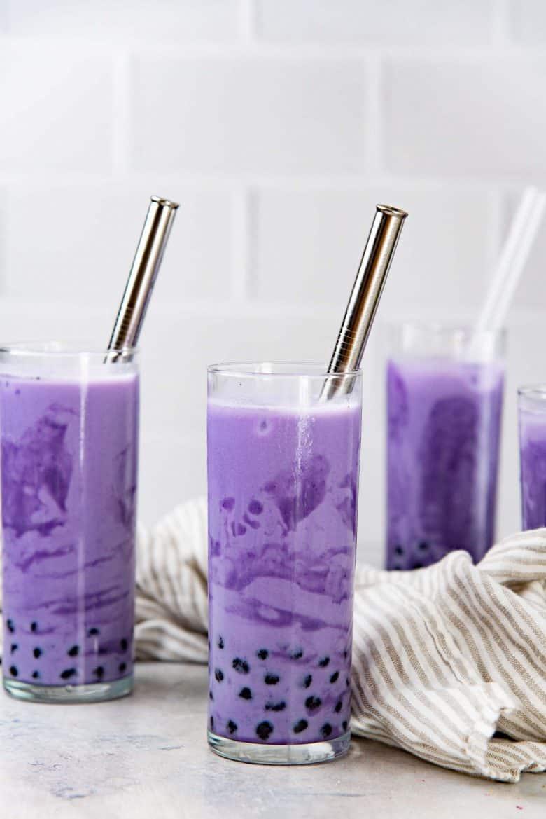 An image of glasses of ube milk with boba straws on a table top.