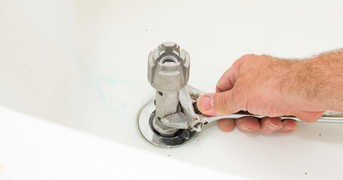 Man using specialty drain wrench to fix bathtub drain leaking.