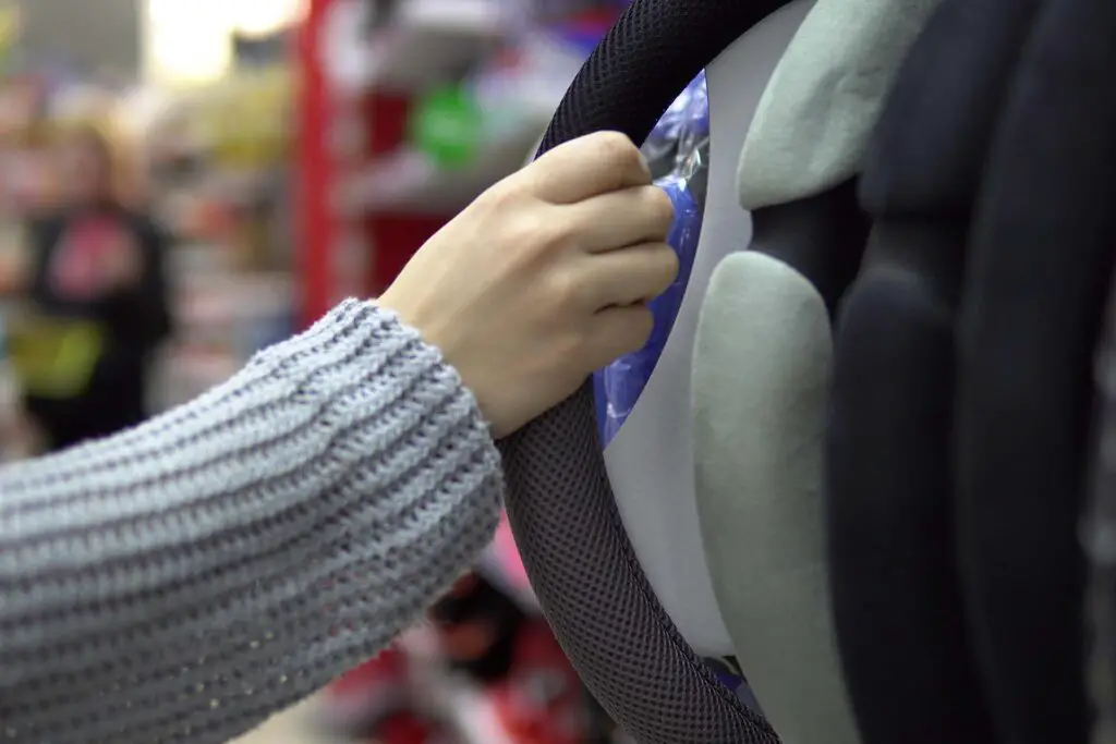 Hand holds automobile steering wheel cover in department of spare parts for autos. Young human chooses new accessories for his car.