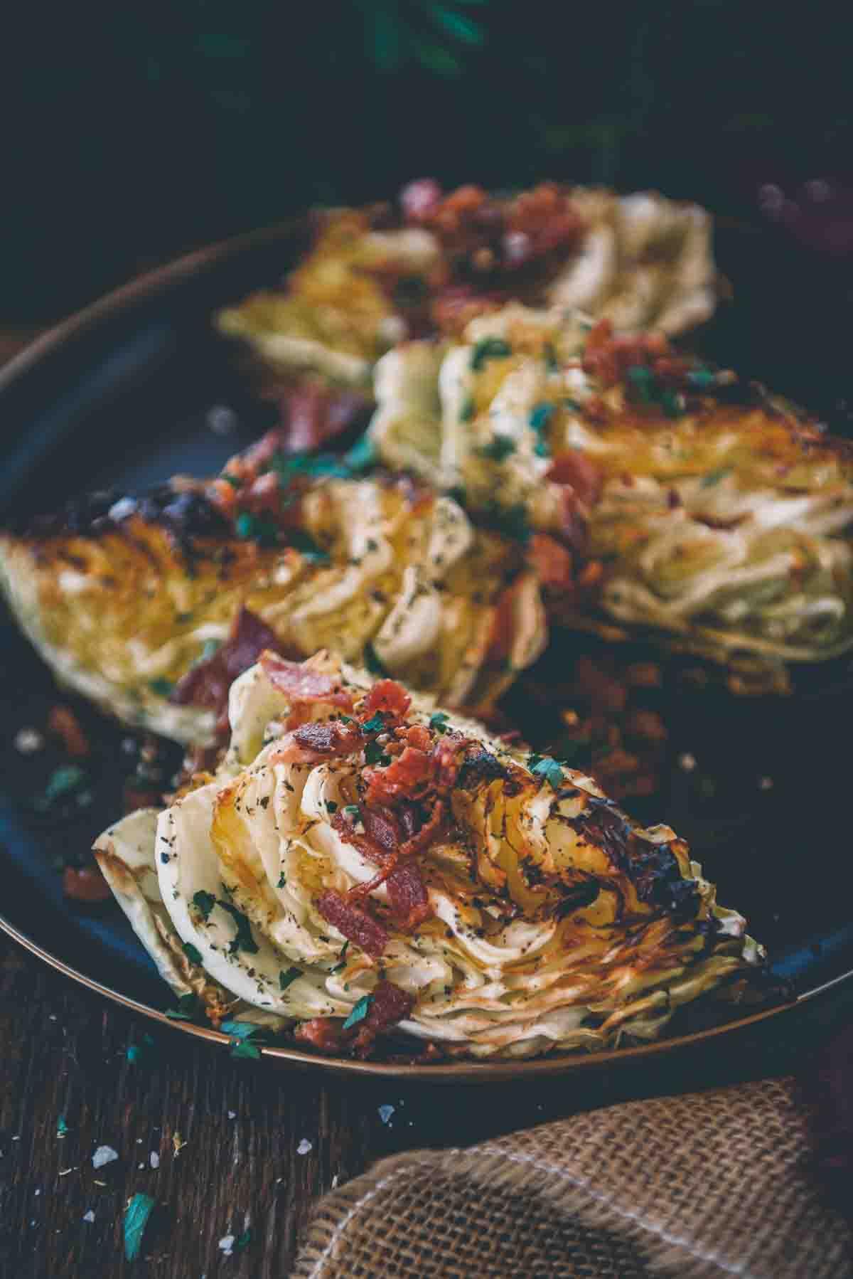 Close up of smoked cabbage with golden brown crispy edges, topped with bacon and parsley.