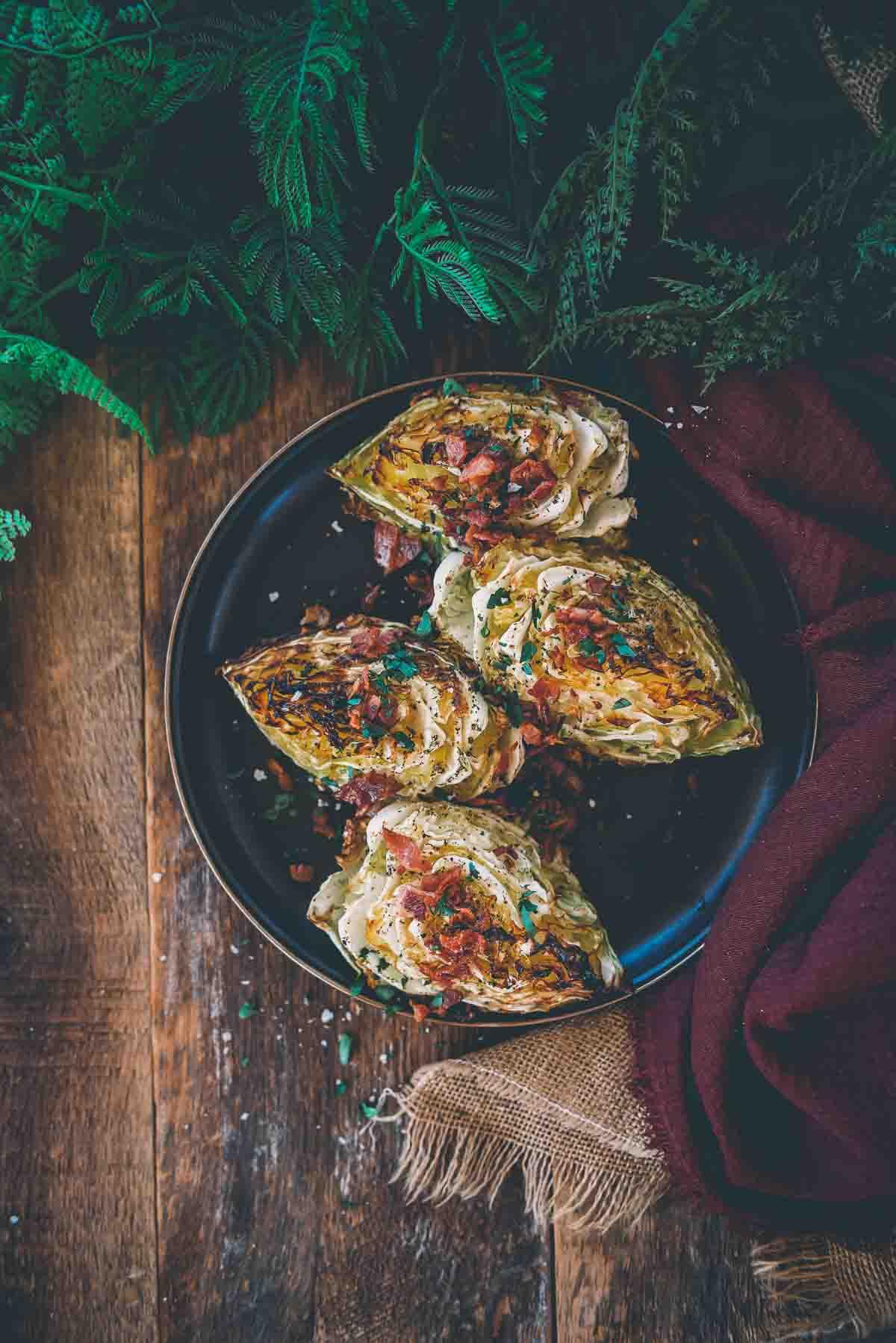 Above shot of smoked cabbage wedges lined up on a platter garnished with bacon and parsley.