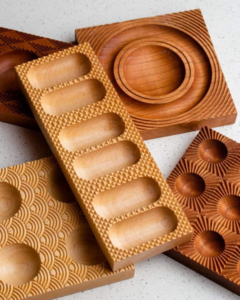 Five wooden ravioli molds on a white bench top.