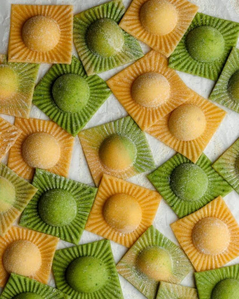 Lots of mini ravioli on white parchment paper. Green and yellow dough.