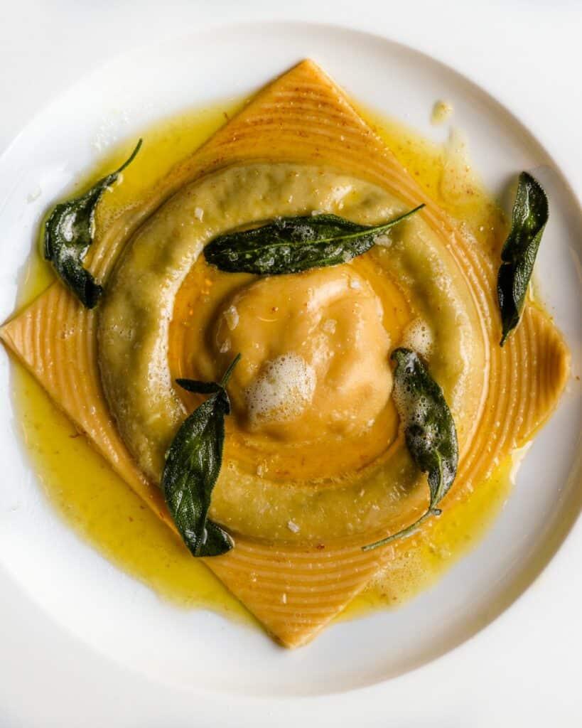 White plate with single raviolo in a sage butter sauce.