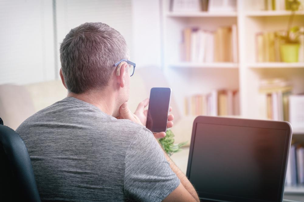 Hearing impaired man working with laptop and mobile phone at home or office.