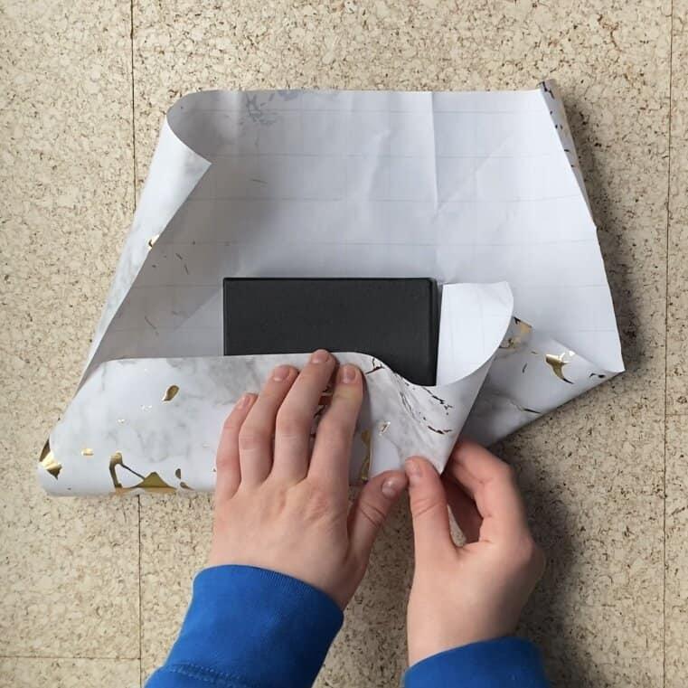 Wrapping a jewelry package in wrapping paper to put a card on the outside.