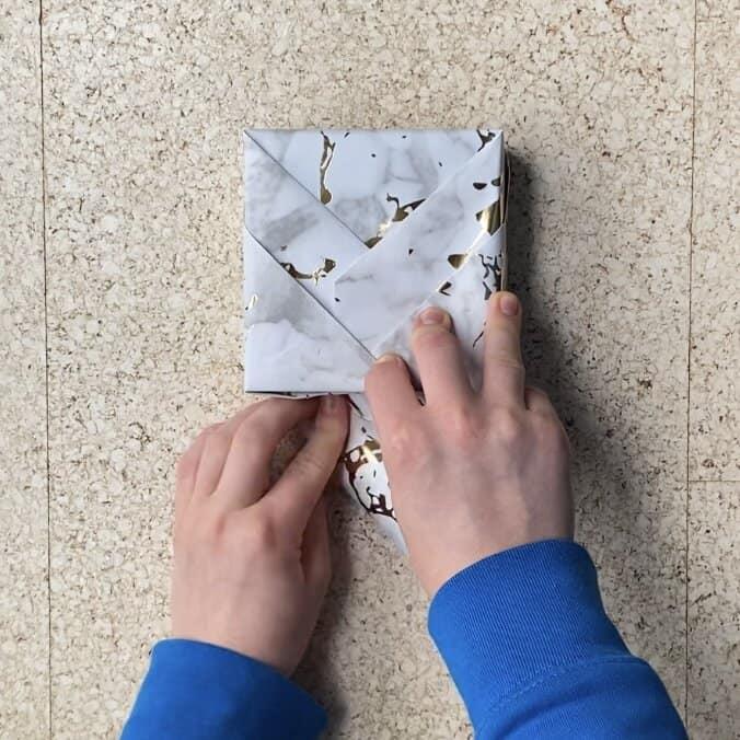 Wrapping a jewelry package in wrapping paper to put a card on the outside.